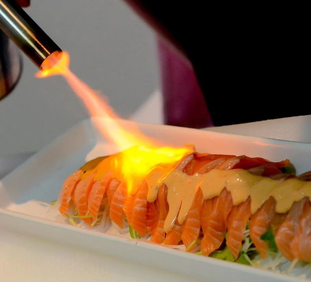 Salmon sashimi being seared with a torch flame